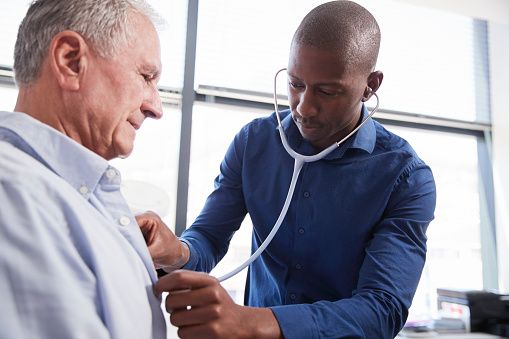 Doctor Listening To Chest Of Senior Male Patient During Medical Exam In Office